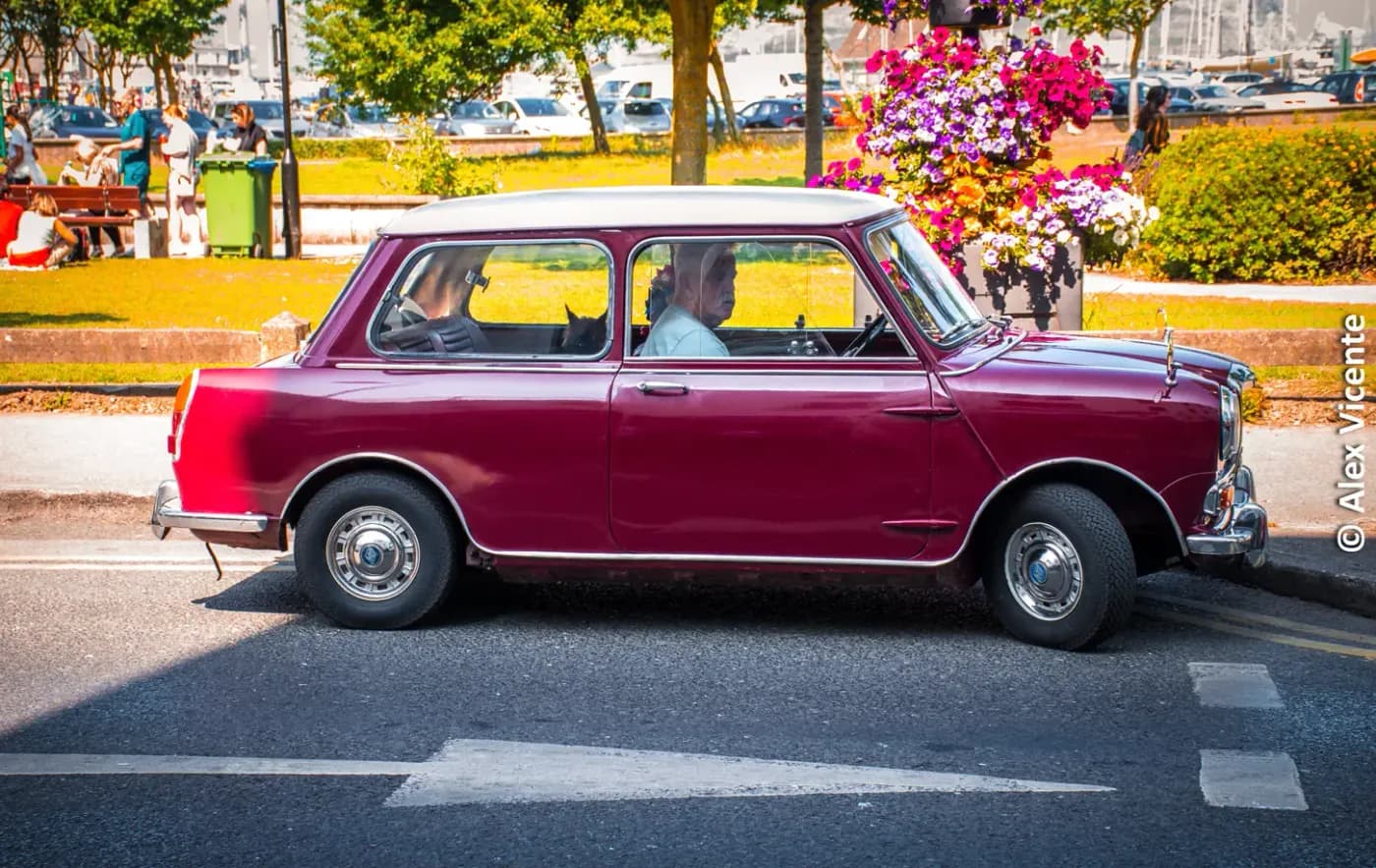 Burgundy classic car moving through a sunlit street